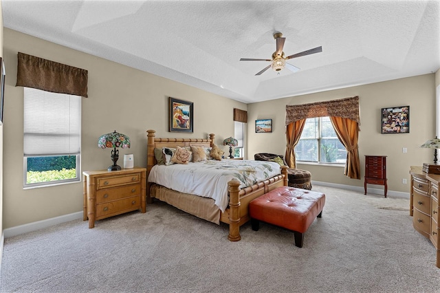 bedroom featuring baseboards, ceiling fan, light colored carpet, a textured ceiling, and a raised ceiling