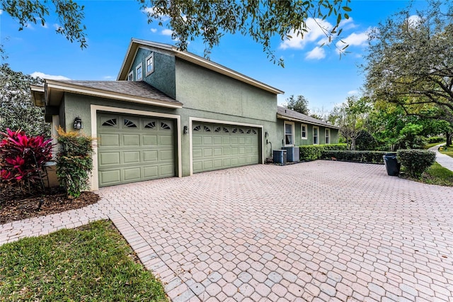 view of side of home with central AC unit, stucco siding, decorative driveway, and a garage