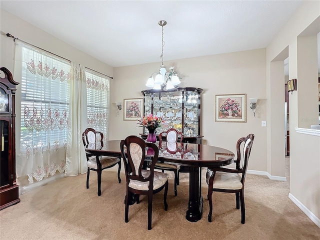 dining room with a chandelier, light colored carpet, and baseboards