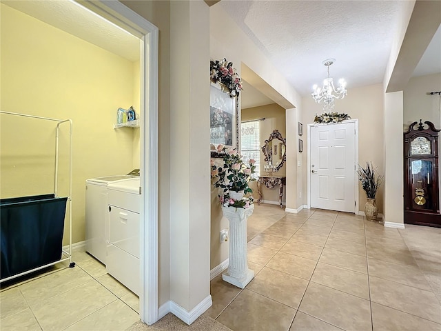 foyer with light tile patterned floors, a textured ceiling, a notable chandelier, baseboards, and washer and dryer