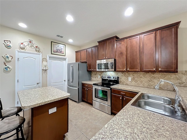 kitchen featuring a breakfast bar, a sink, visible vents, appliances with stainless steel finishes, and tasteful backsplash