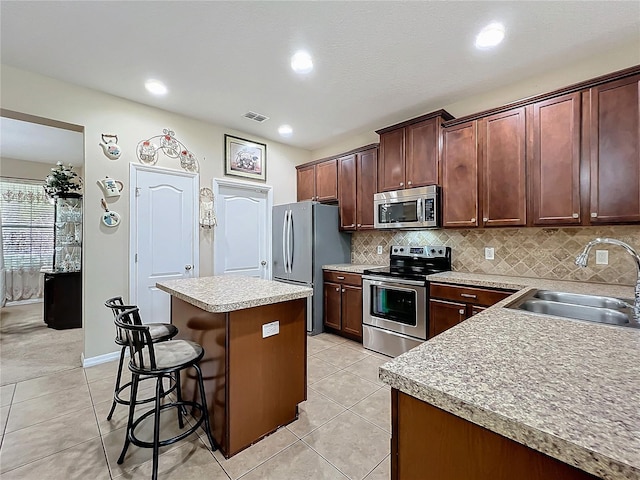 kitchen featuring stainless steel appliances, a sink, visible vents, a center island, and a kitchen bar