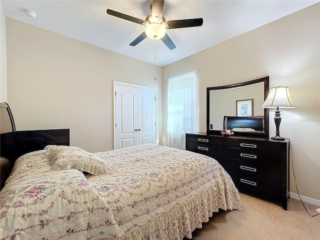 bedroom featuring a textured ceiling, light colored carpet, a ceiling fan, baseboards, and a closet