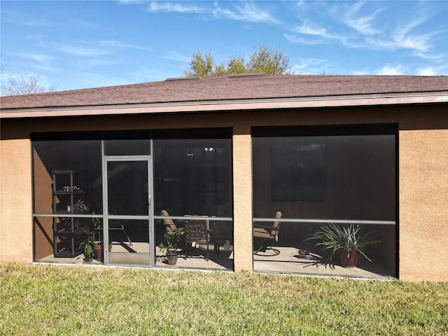 back of property featuring a sunroom, a shingled roof, a lawn, and stucco siding