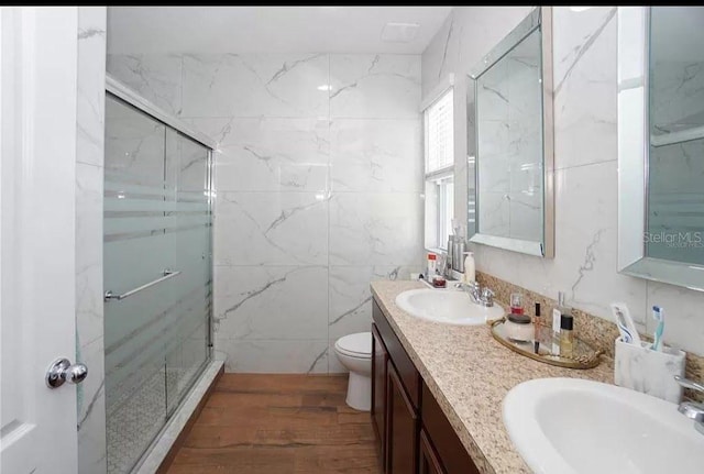 full bath with toilet, double vanity, a marble finish shower, and a sink