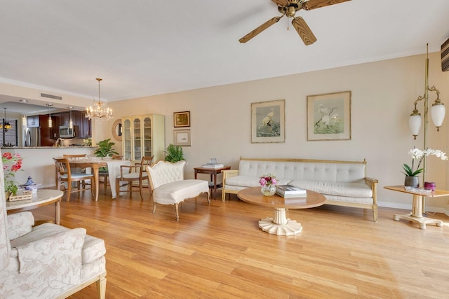 living room featuring visible vents, ceiling fan with notable chandelier, light wood-style floors, and ornamental molding