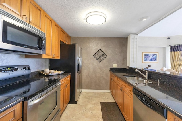 kitchen featuring a sink, stainless steel appliances, brown cabinetry, and a textured wall