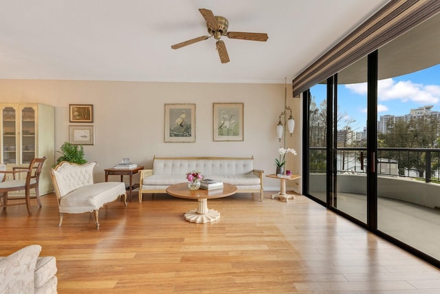 living room featuring a wall of windows, light wood-type flooring, ceiling fan, and ornamental molding