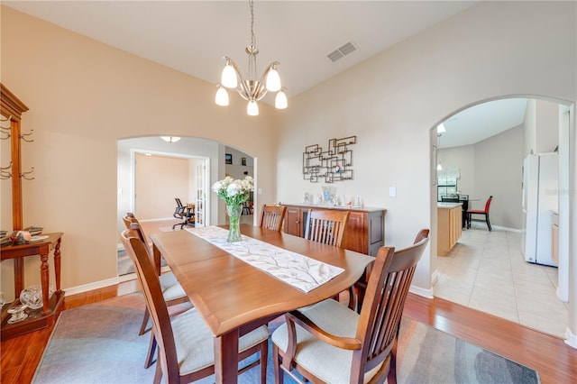 dining space with arched walkways, visible vents, light wood-style flooring, and a notable chandelier