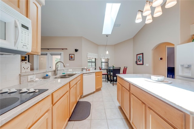 kitchen with light brown cabinets, light tile patterned floors, a skylight, white appliances, and a sink