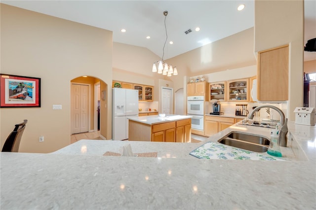 kitchen featuring visible vents, light brown cabinetry, arched walkways, white appliances, and a sink