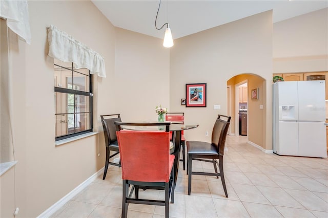 dining space with light tile patterned floors, baseboards, arched walkways, and a towering ceiling