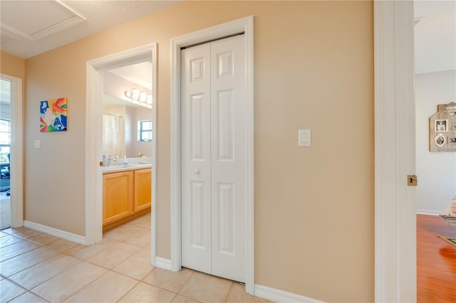 corridor with light tile patterned floors, a healthy amount of sunlight, attic access, and baseboards