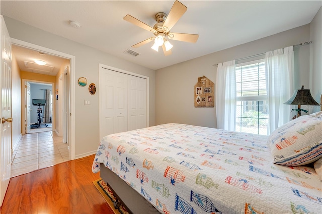 bedroom with light wood-type flooring, visible vents, a ceiling fan, a closet, and attic access