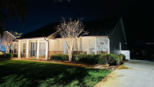 property exterior at night featuring stone siding and a yard