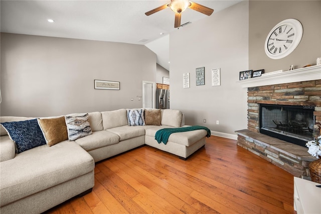 living area with lofted ceiling, a fireplace, visible vents, a ceiling fan, and light wood finished floors