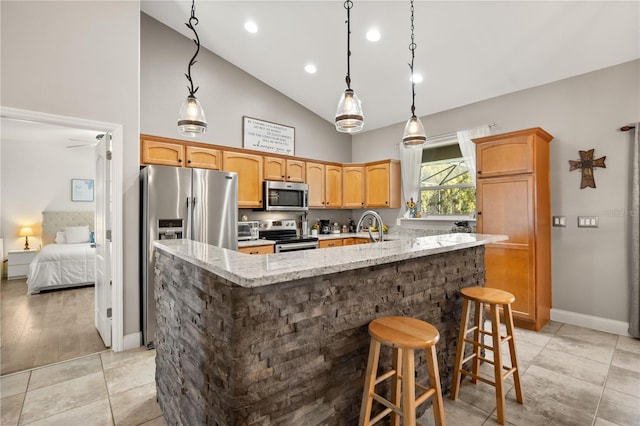 kitchen with a sink, appliances with stainless steel finishes, light stone countertops, an island with sink, and a kitchen bar