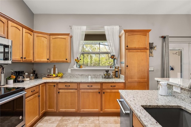 kitchen featuring appliances with stainless steel finishes, brown cabinetry, a sink, and light stone countertops