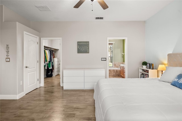 bedroom featuring visible vents, connected bathroom, ceiling fan, wood finished floors, and a walk in closet