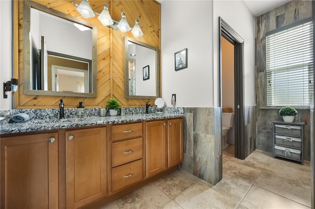 bathroom with toilet, double vanity, a sink, and tile walls