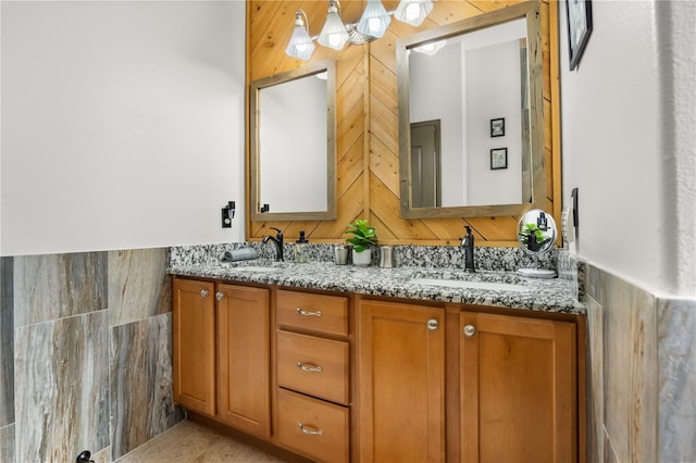 bathroom with wainscoting, a sink, tile walls, and double vanity