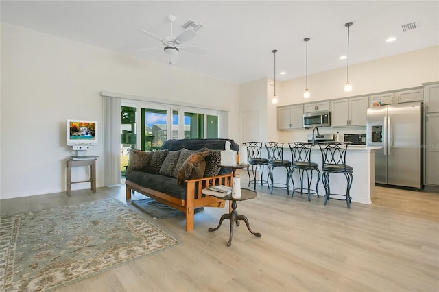 living room featuring visible vents, light wood-style flooring, and a ceiling fan