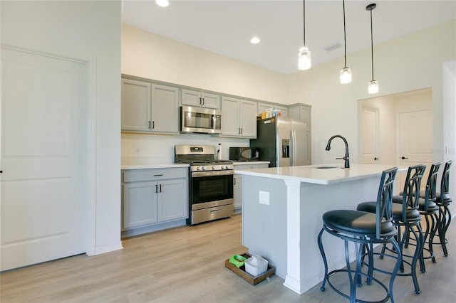 kitchen with gray cabinetry, a sink, light wood-style floors, appliances with stainless steel finishes, and a kitchen breakfast bar