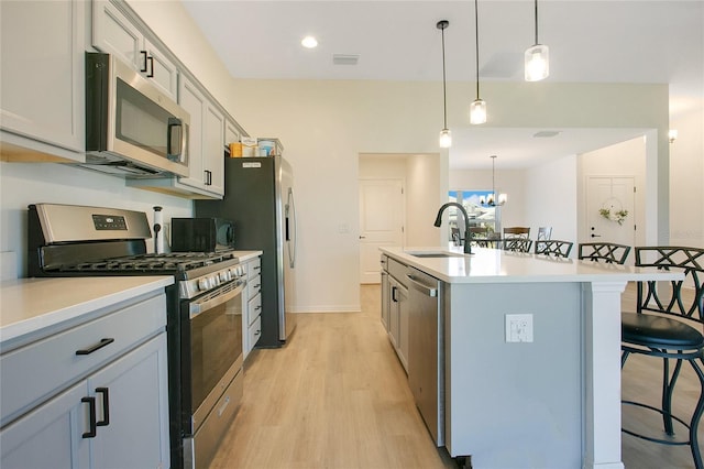 kitchen with a breakfast bar, an island with sink, light wood-style flooring, a sink, and stainless steel appliances