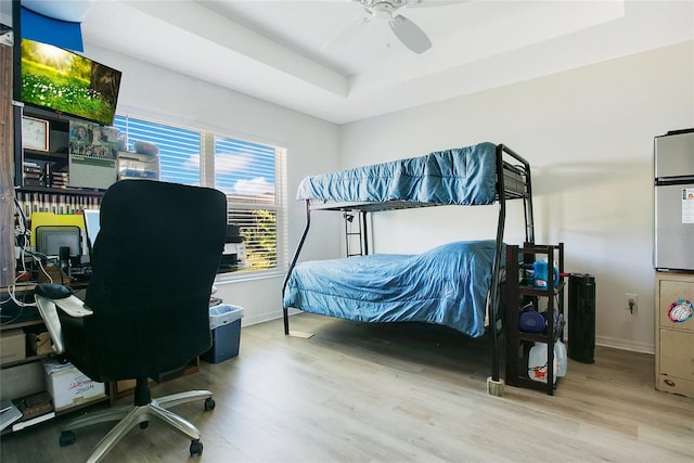 bedroom with a raised ceiling, wood finished floors, baseboards, and ceiling fan