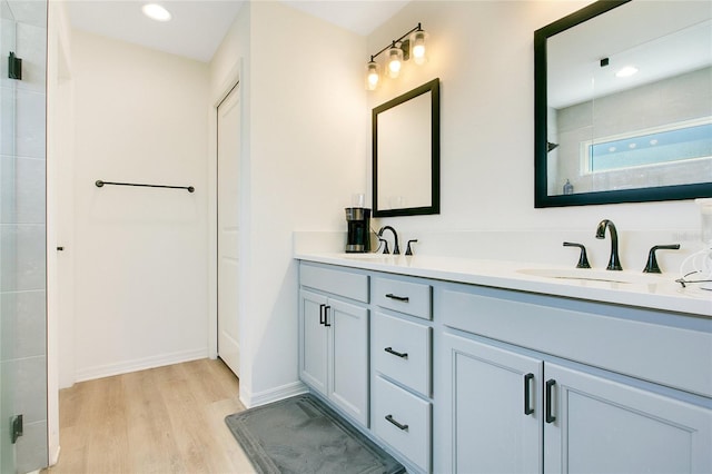 full bathroom featuring double vanity, a tile shower, wood finished floors, and a sink