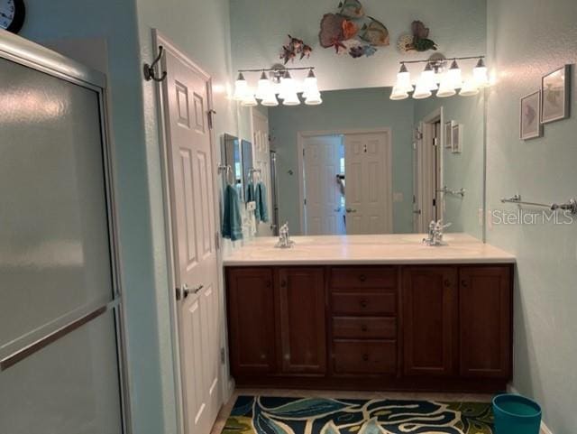 bathroom with a shower with door, double vanity, and a sink