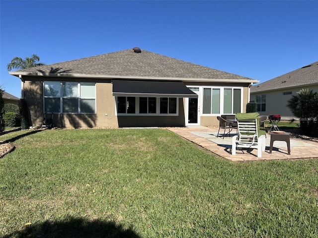 rear view of house with a patio area, stucco siding, a yard, and roof with shingles