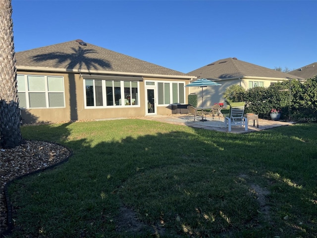 rear view of house with stucco siding, a yard, roof with shingles, and a patio area