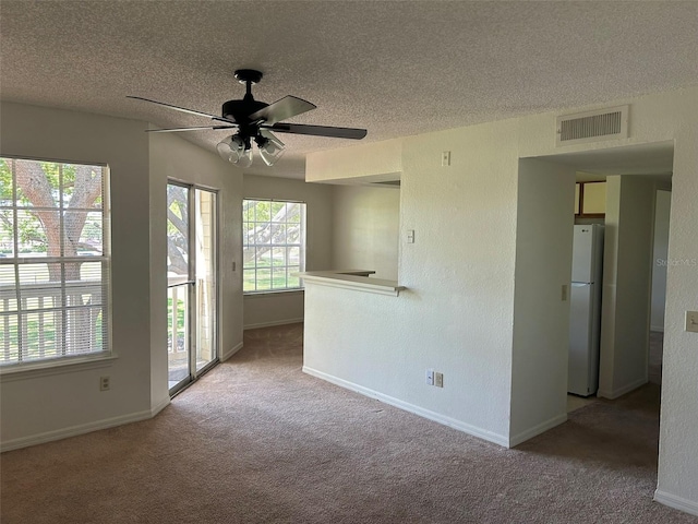 carpeted empty room with a textured ceiling, ceiling fan, visible vents, and baseboards