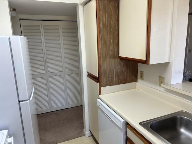 kitchen with light carpet, white appliances, a sink, white cabinetry, and light countertops