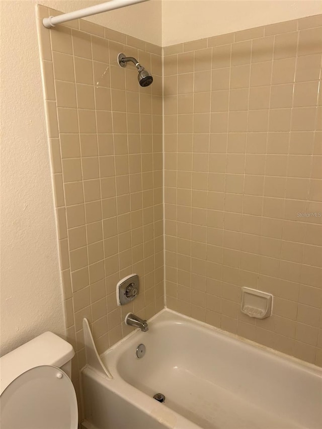 bathroom featuring toilet, tub / shower combination, and a textured wall