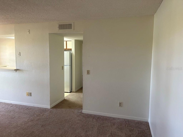 carpeted empty room with baseboards, visible vents, and a textured ceiling