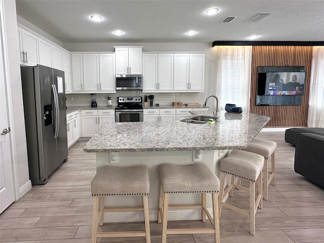 kitchen featuring stainless steel appliances, a sink, visible vents, decorative backsplash, and wood tiled floor