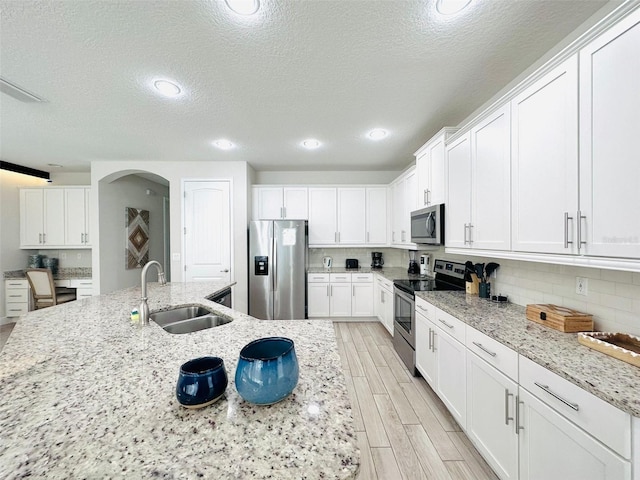 kitchen with arched walkways, appliances with stainless steel finishes, wood tiled floor, white cabinetry, and a sink