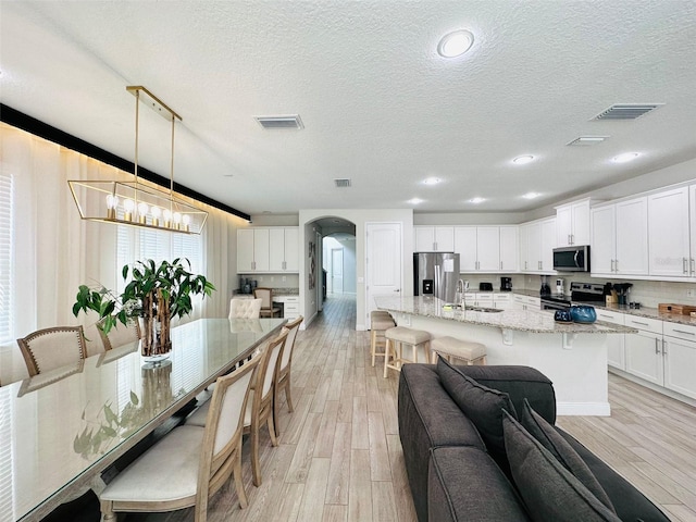dining area featuring arched walkways, visible vents, and light wood-style flooring