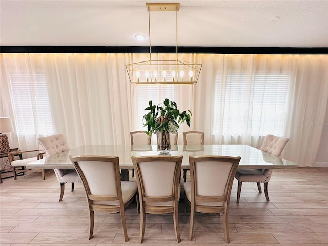 dining space with a wealth of natural light, a notable chandelier, a textured ceiling, and light wood finished floors