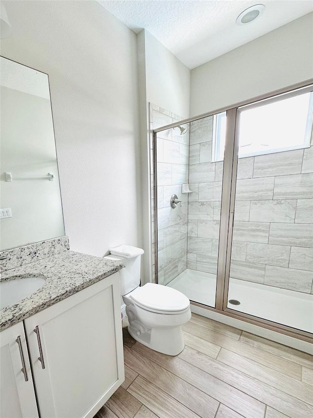 bathroom featuring toilet, vanity, a textured ceiling, wood finish floors, and a shower stall