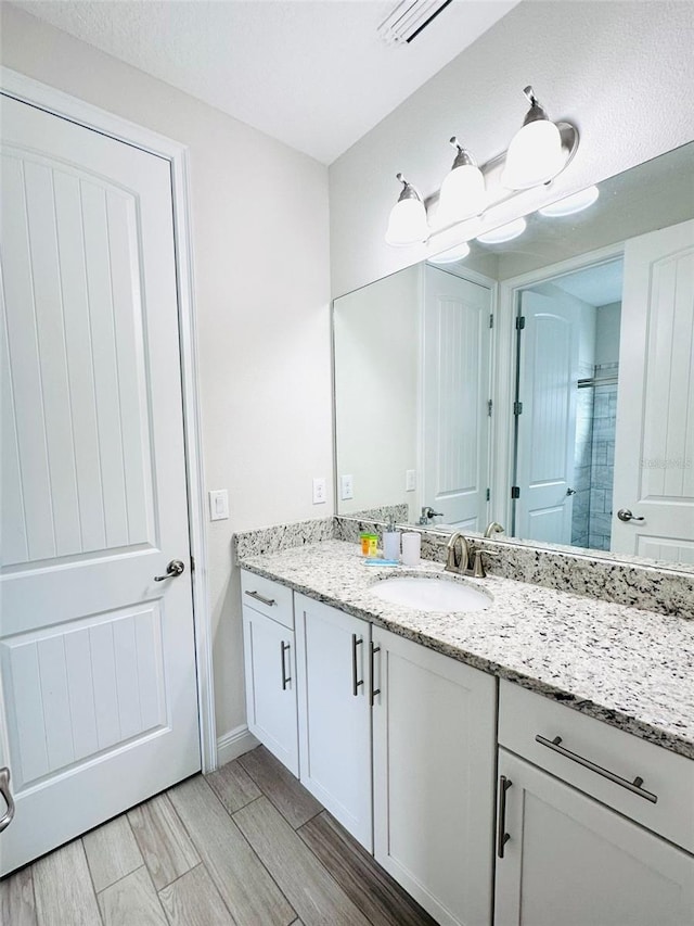 full bathroom featuring baseboards, visible vents, tiled shower, vanity, and wood finish floors