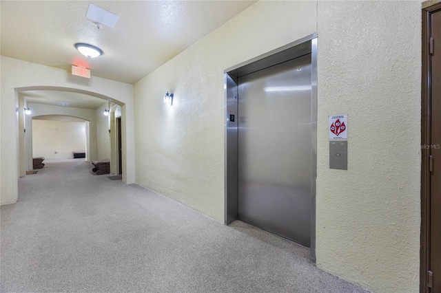 hall with arched walkways, carpet, a textured wall, elevator, and a textured ceiling