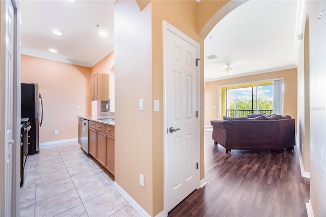 corridor featuring light tile patterned floors, baseboards, arched walkways, crown molding, and recessed lighting