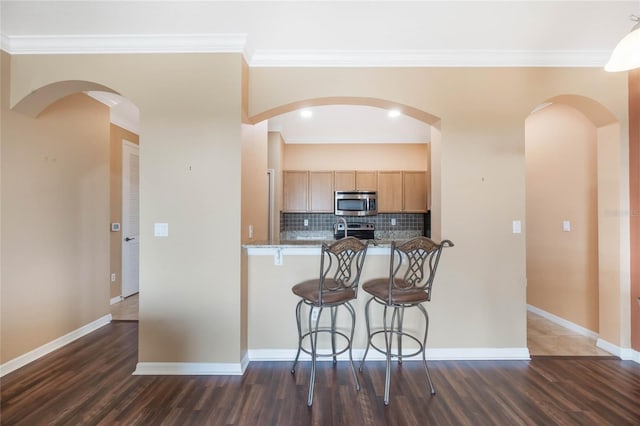 kitchen featuring a breakfast bar area, stainless steel appliances, baseboards, decorative backsplash, and light brown cabinetry