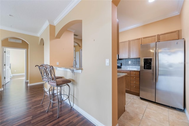 kitchen featuring a breakfast bar, light stone countertops, crown molding, stainless steel refrigerator with ice dispenser, and backsplash