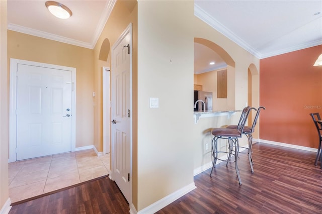 hall with arched walkways, crown molding, baseboards, and wood finished floors