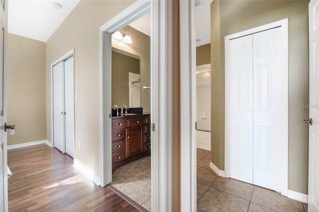 corridor featuring light tile patterned floors, a sink, and baseboards