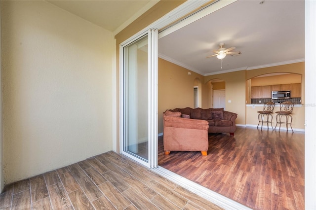 living area featuring ornamental molding, arched walkways, a ceiling fan, and wood finished floors